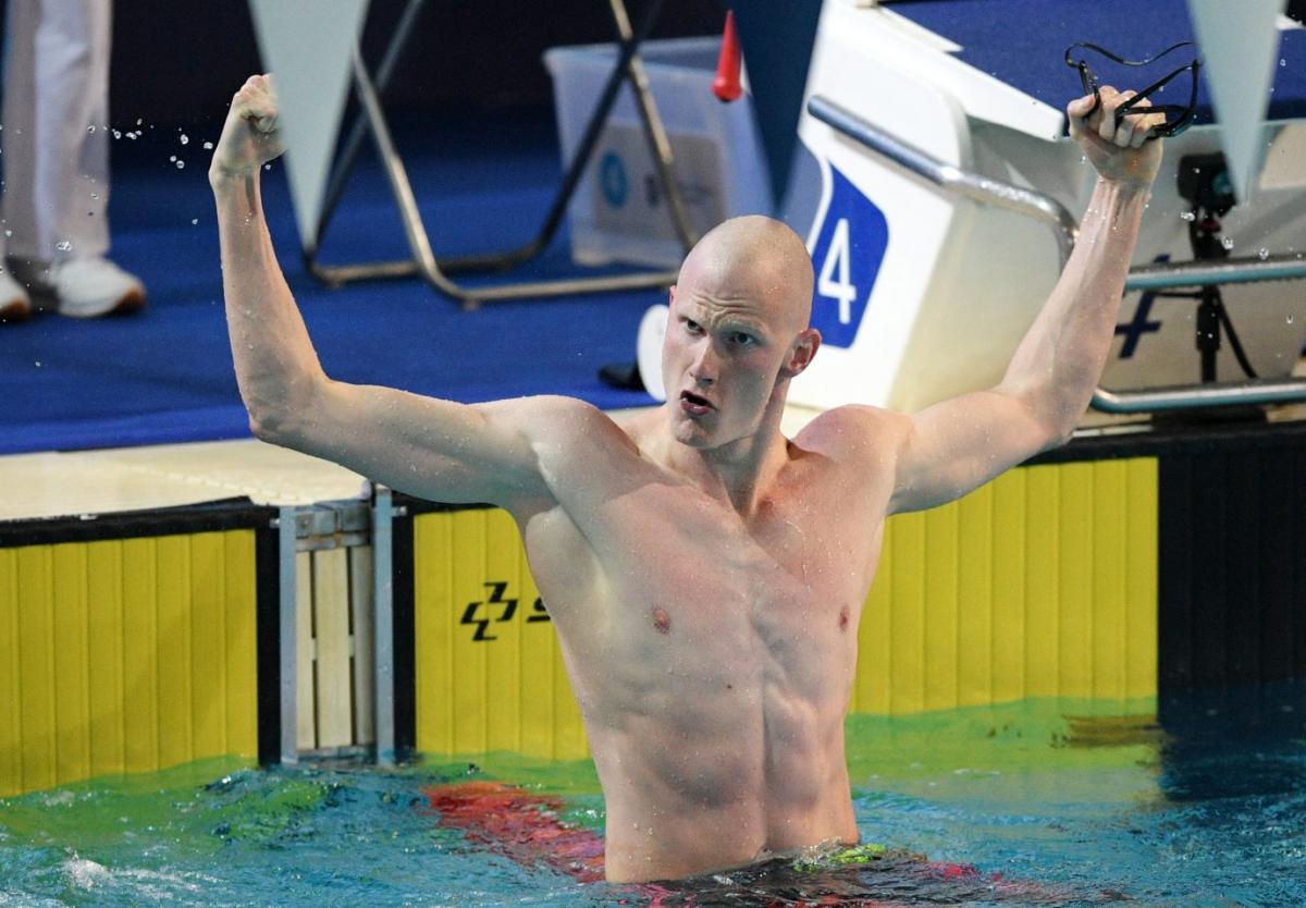 A male swimmer open his arms to celebrate in the pool