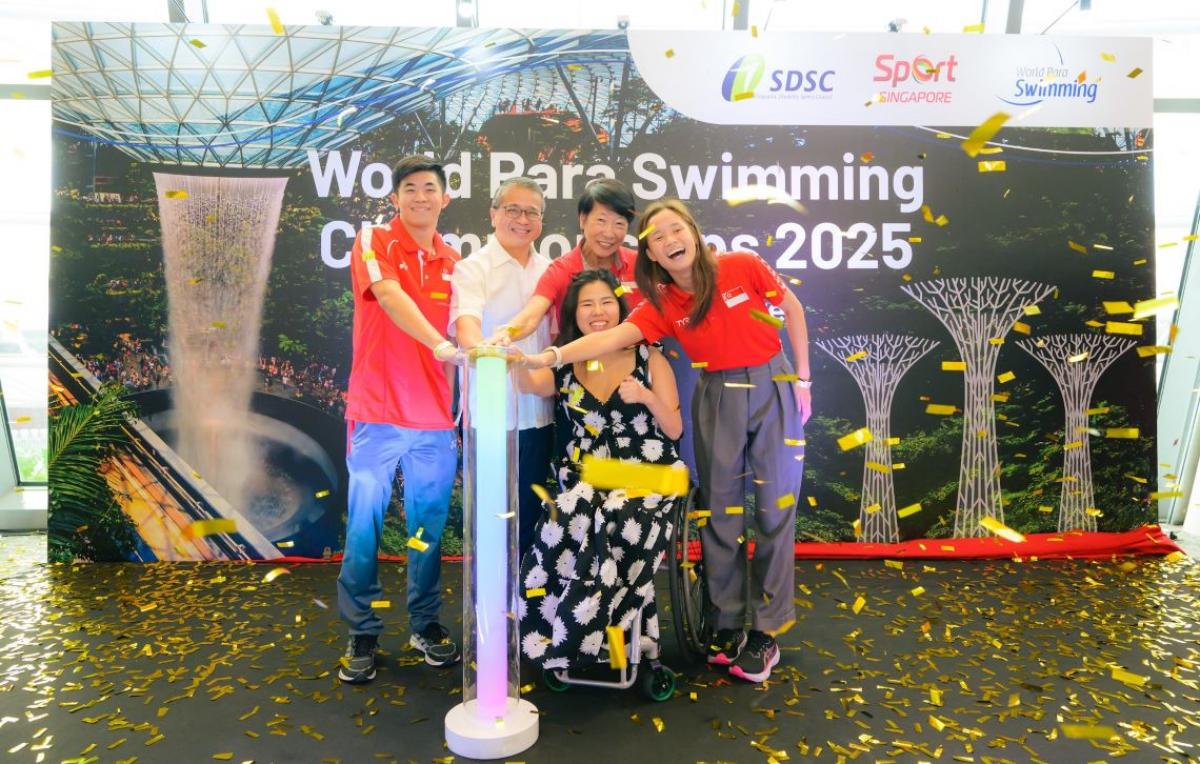 A woman in a wheelchair and four persons standing pressing a button