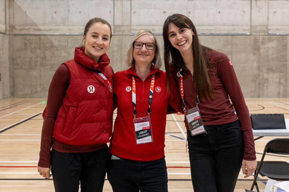 Three women wearing Canada's red uniforms pose for a photo