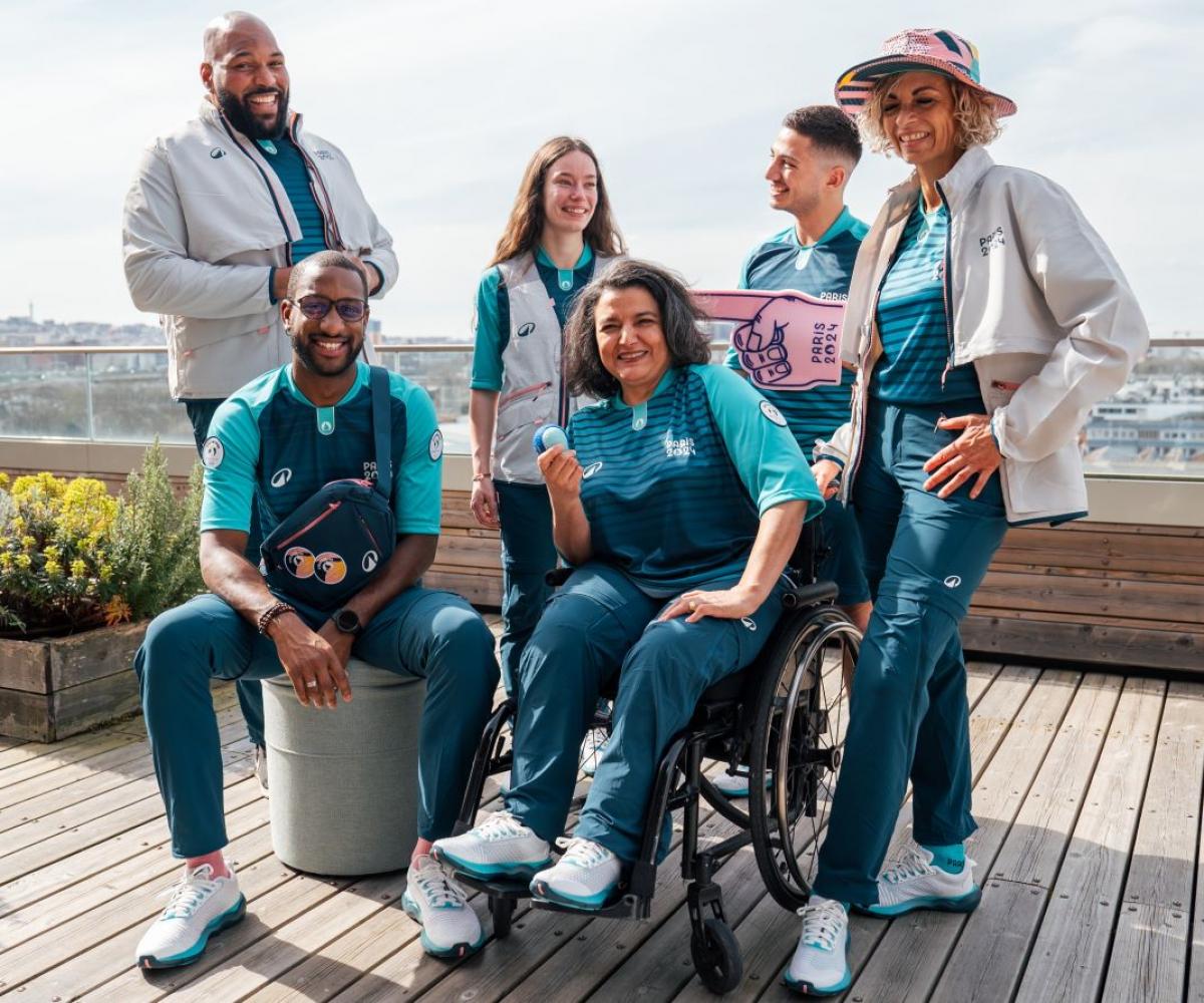 Six male and female volunteers pose for a photograph wearing the Paris 2024 volunteer uniform.