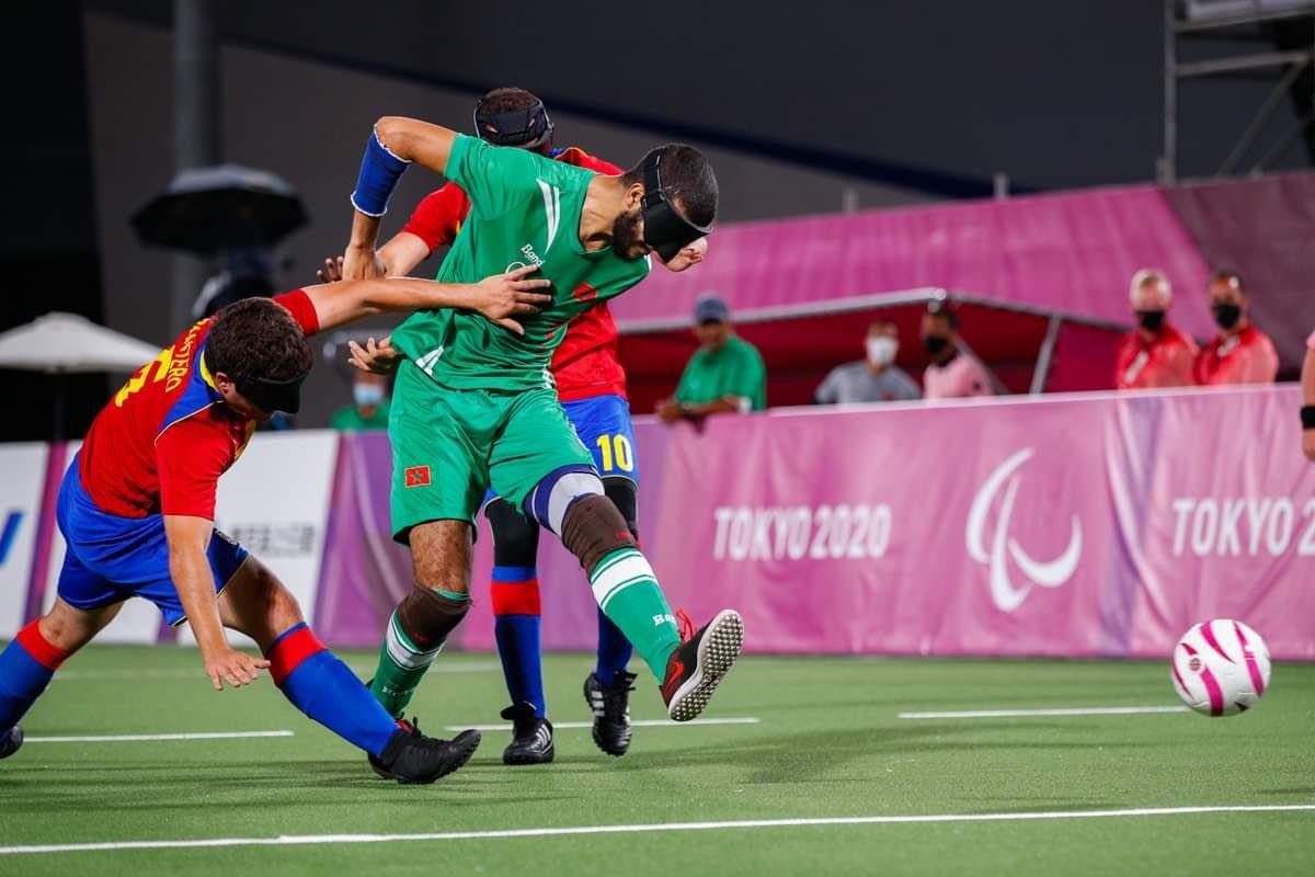 A male blind football player wearing a green uniform runs past two players