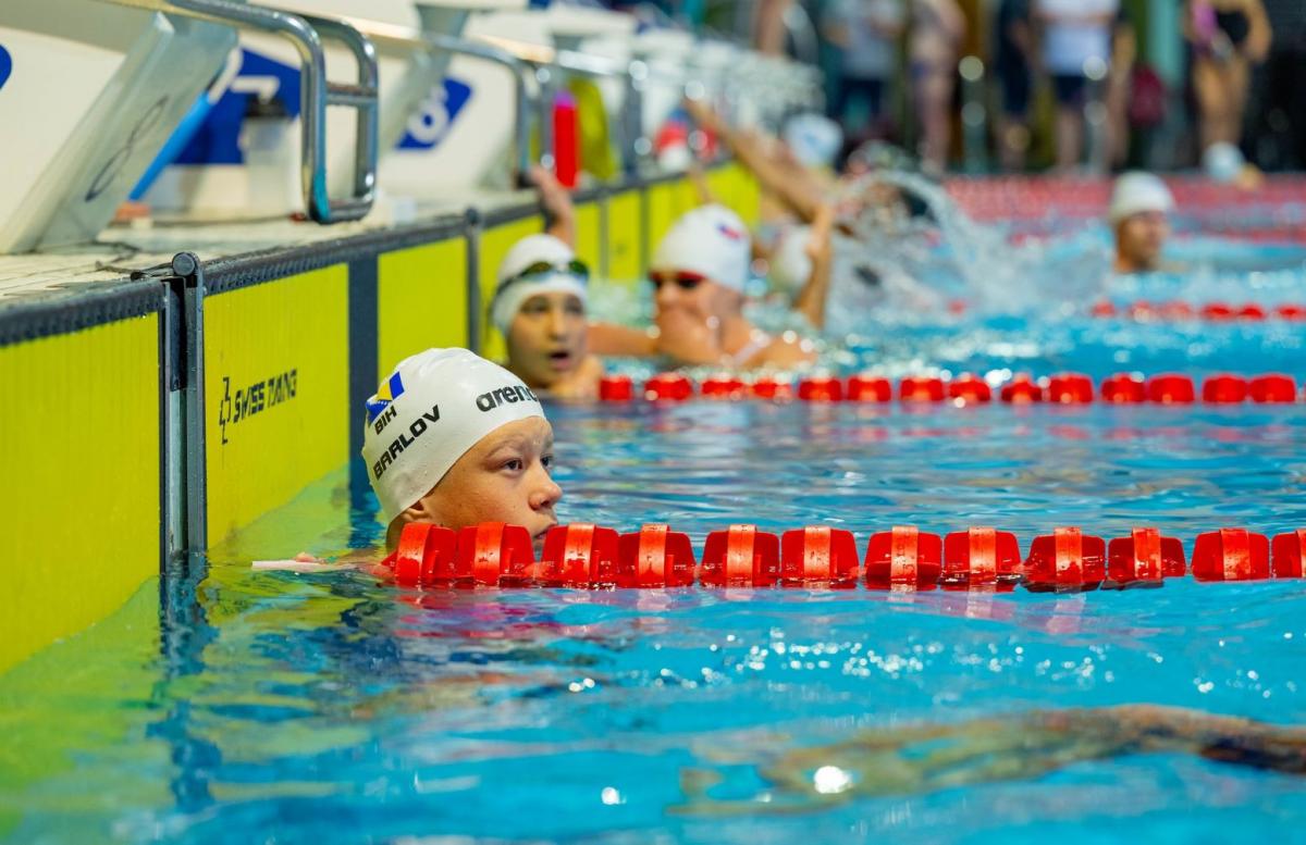 A male swimmer in a swimming pool lane with other swimmers in the background