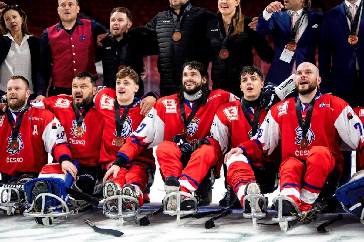 A group of Para ice hockey players with a group of standing people behind them