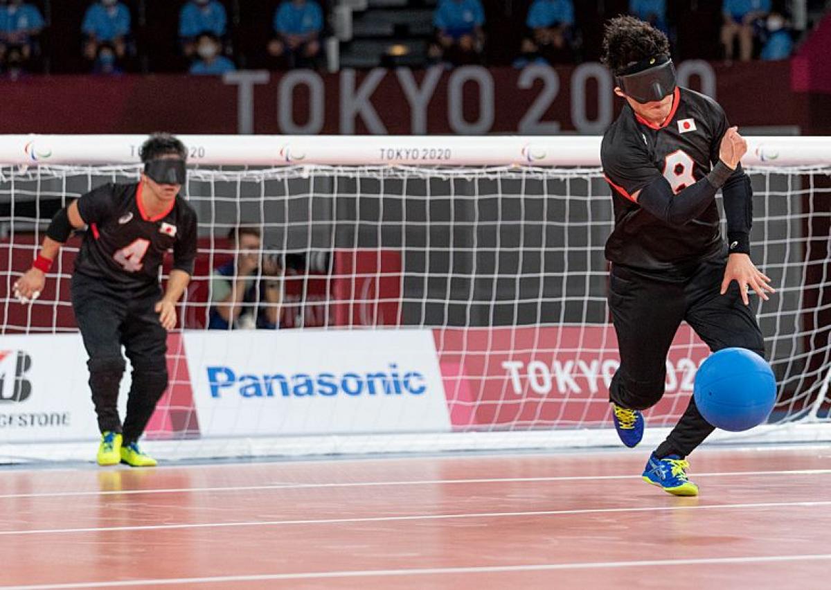 A male goalball player rolls the blue goalball in front of his net.