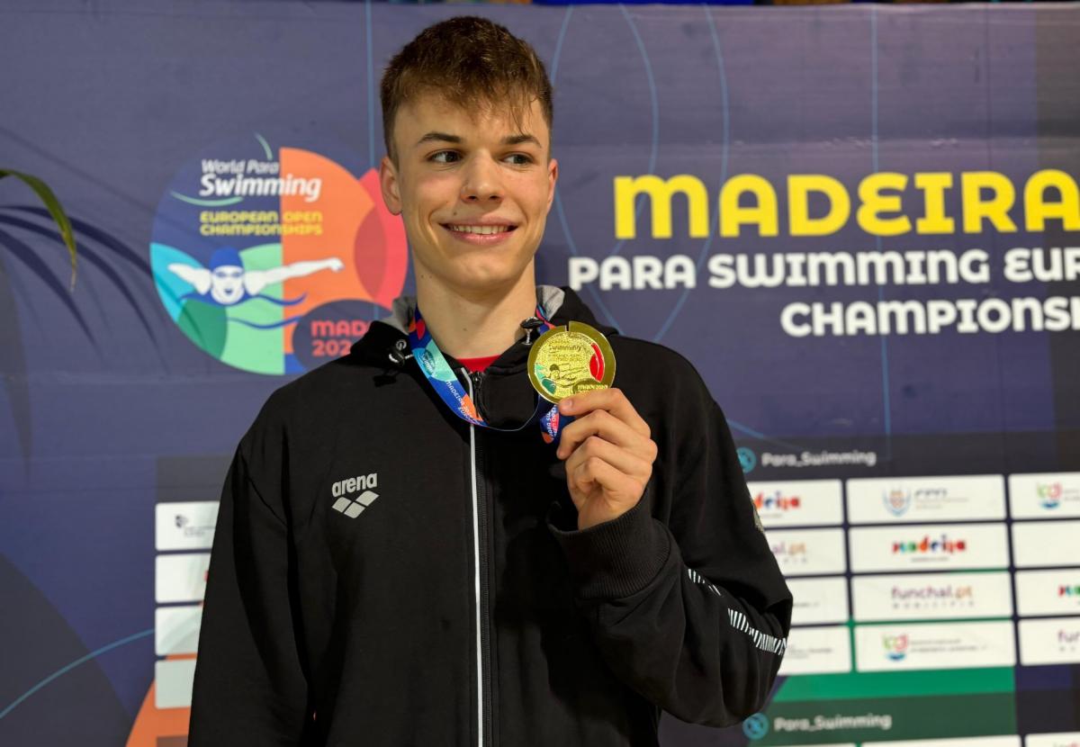 A man showing his gold medal on a podium