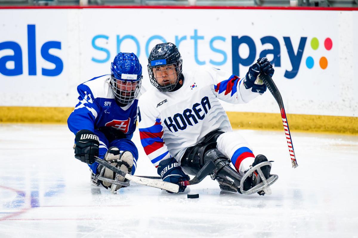 Two Para ice hockey players trying to reach the puck