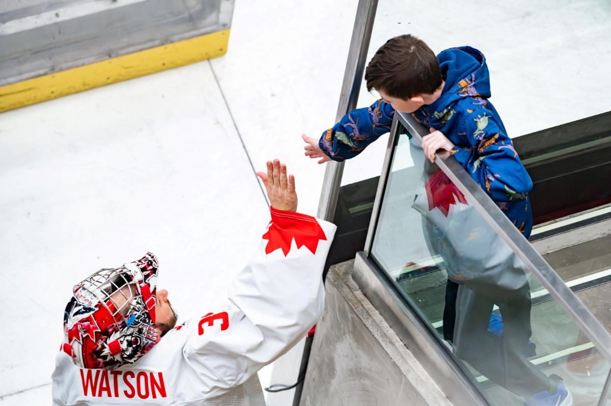 A hockey goaltender high-fiving a young fan in a rink