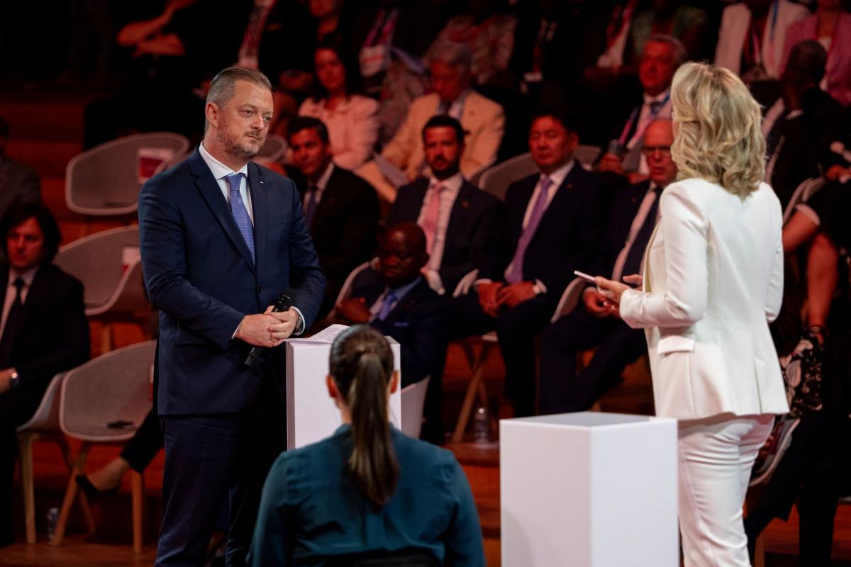 Andrew Parsons, IPC President, stands on the stage with two participants. People