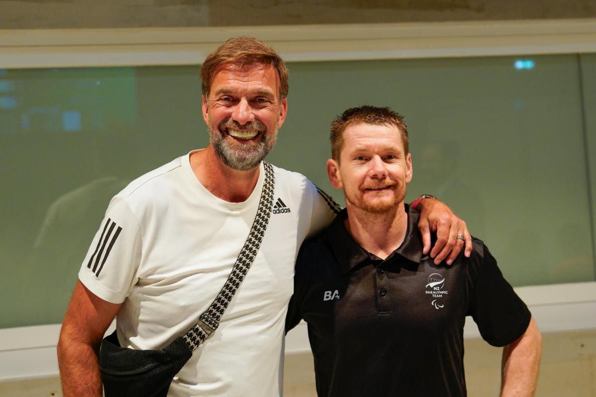 Man in a white tee with his arm round man in a black tee 