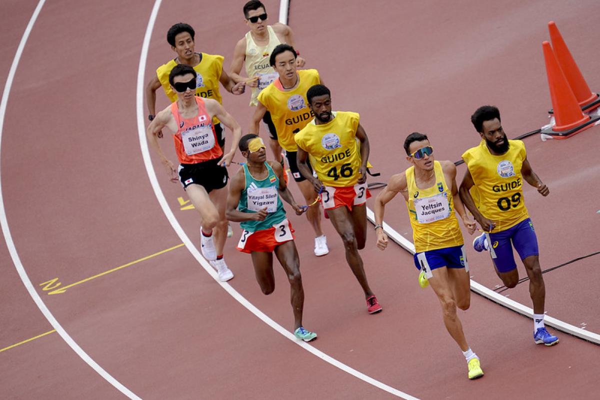 A runner and his guide ahead of three other runners with guides in a race