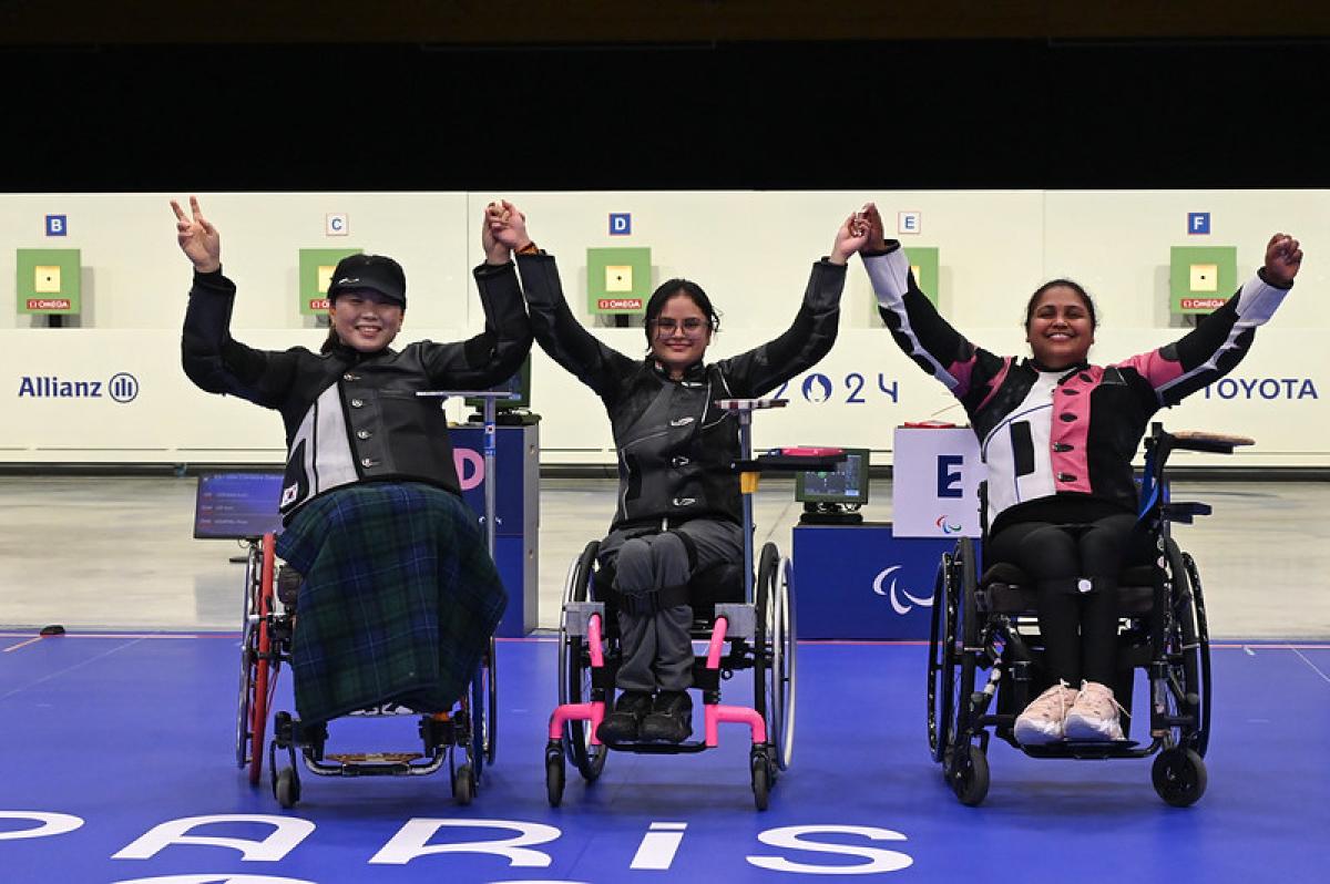 Three women in wheelchairs holding hands in a shooting range