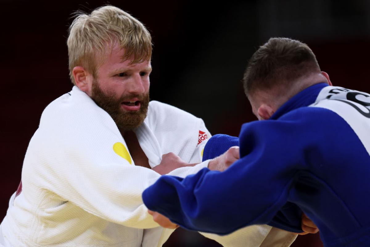 Two male judo athletes are grappling, grabbing their judogis during competition