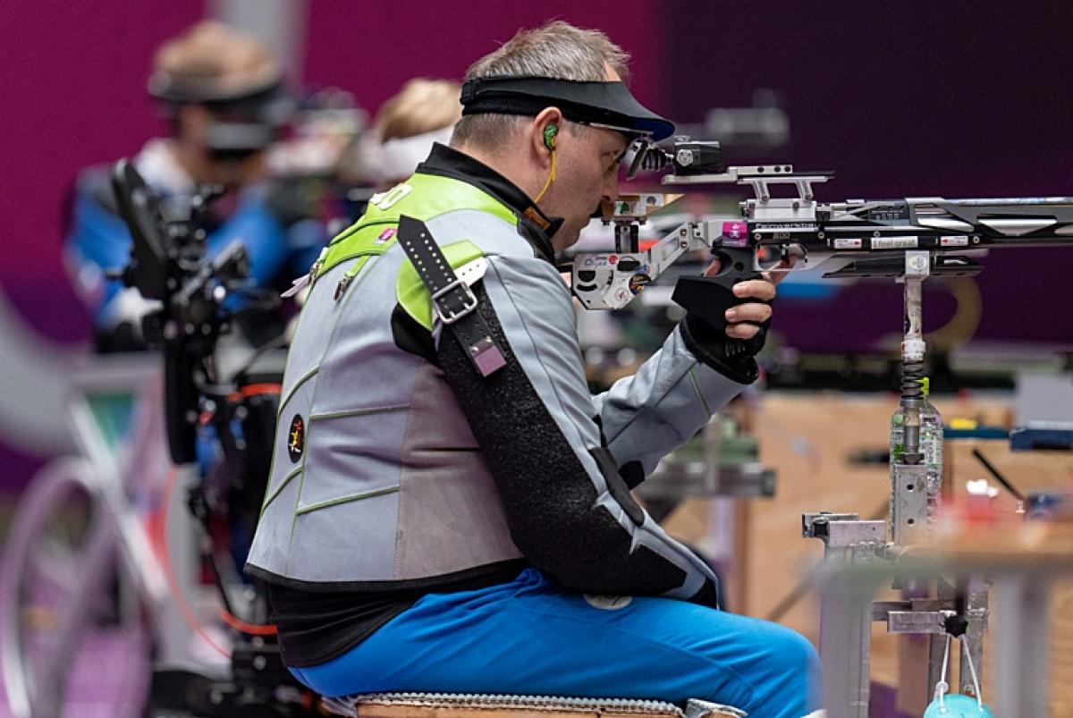 A male athlete competing in a shooting Para sport range in front of other athletes
