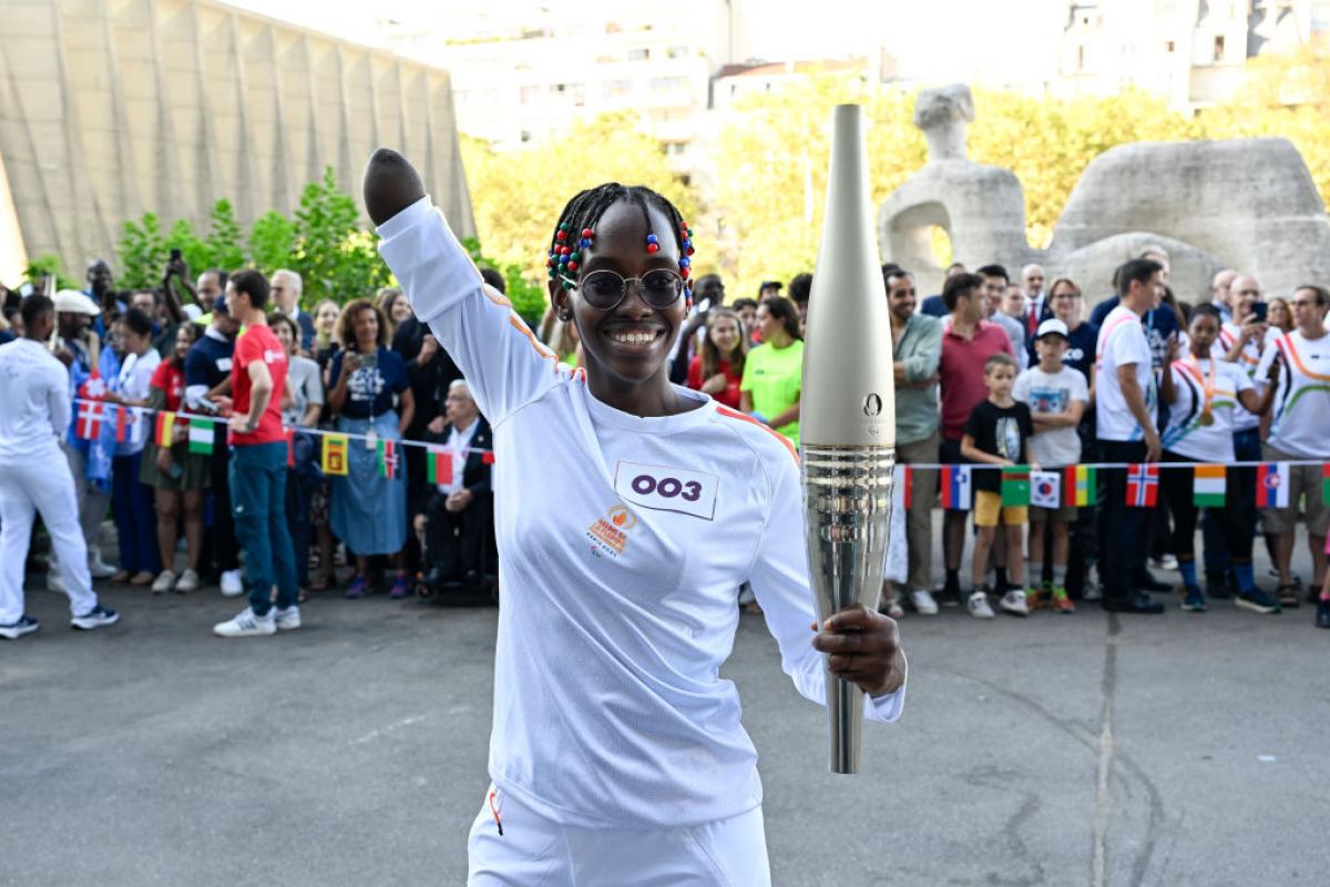 Para swimmer Husnah Kukundakwe holding the Paris 2024 torch and smiling with her arm in the air