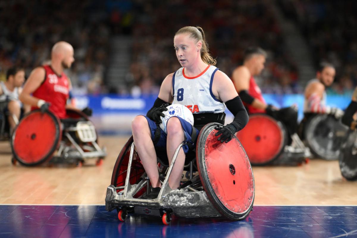 Woman in a white USA tea in wheelchair with red wheels holding a rugby ball