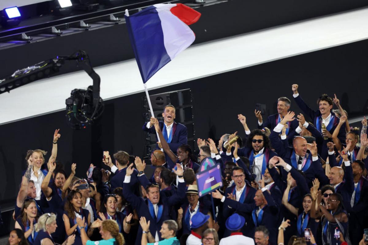 French athletes taking part in the Paris 2024 Parade of Nations. A male athlete is waving the French flag.
