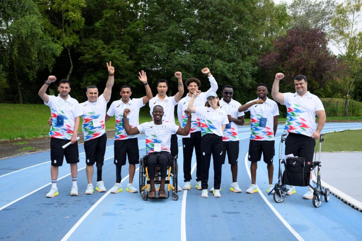 Ten people - eight athletes and two guide runners - pose for a photo on a track. They are wearing watching uniforms