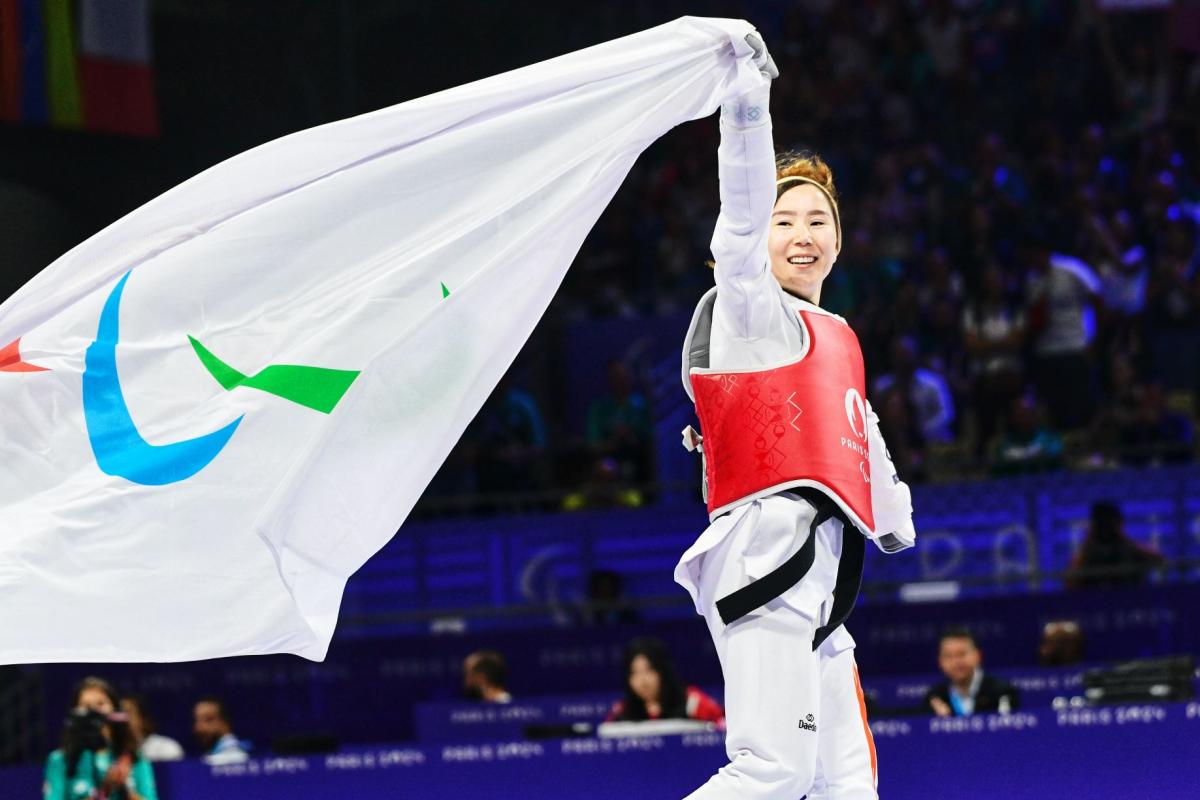Zakia Khudadadi, a female Para taekwondo athlete, runs while holding the Paralympic flag with her right hand