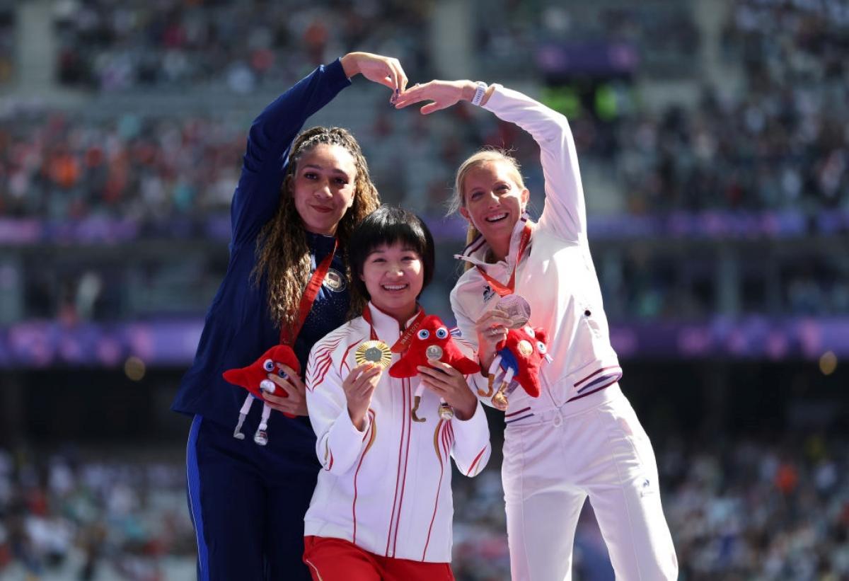Three women on a podium celebrating their medals