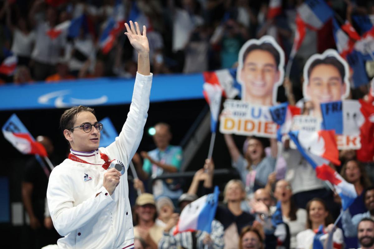 A young man with a medal waving to the crowd in an indoor arena