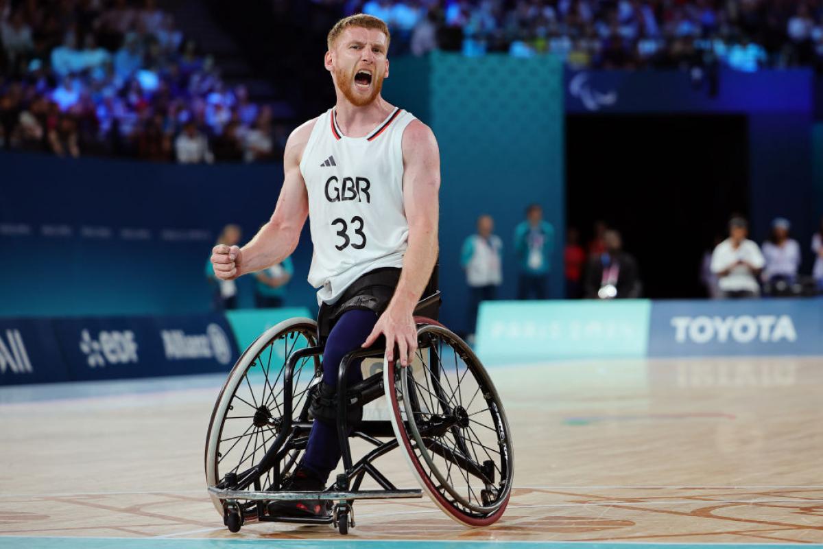 A man in a Great Britain uniform and a basketball wheelchair yells in celebration