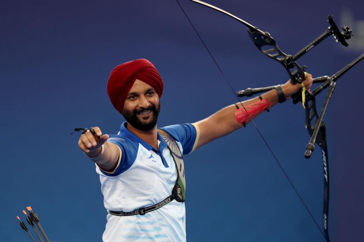 A man raises both arms in the air, carrying an archery bow in one hand