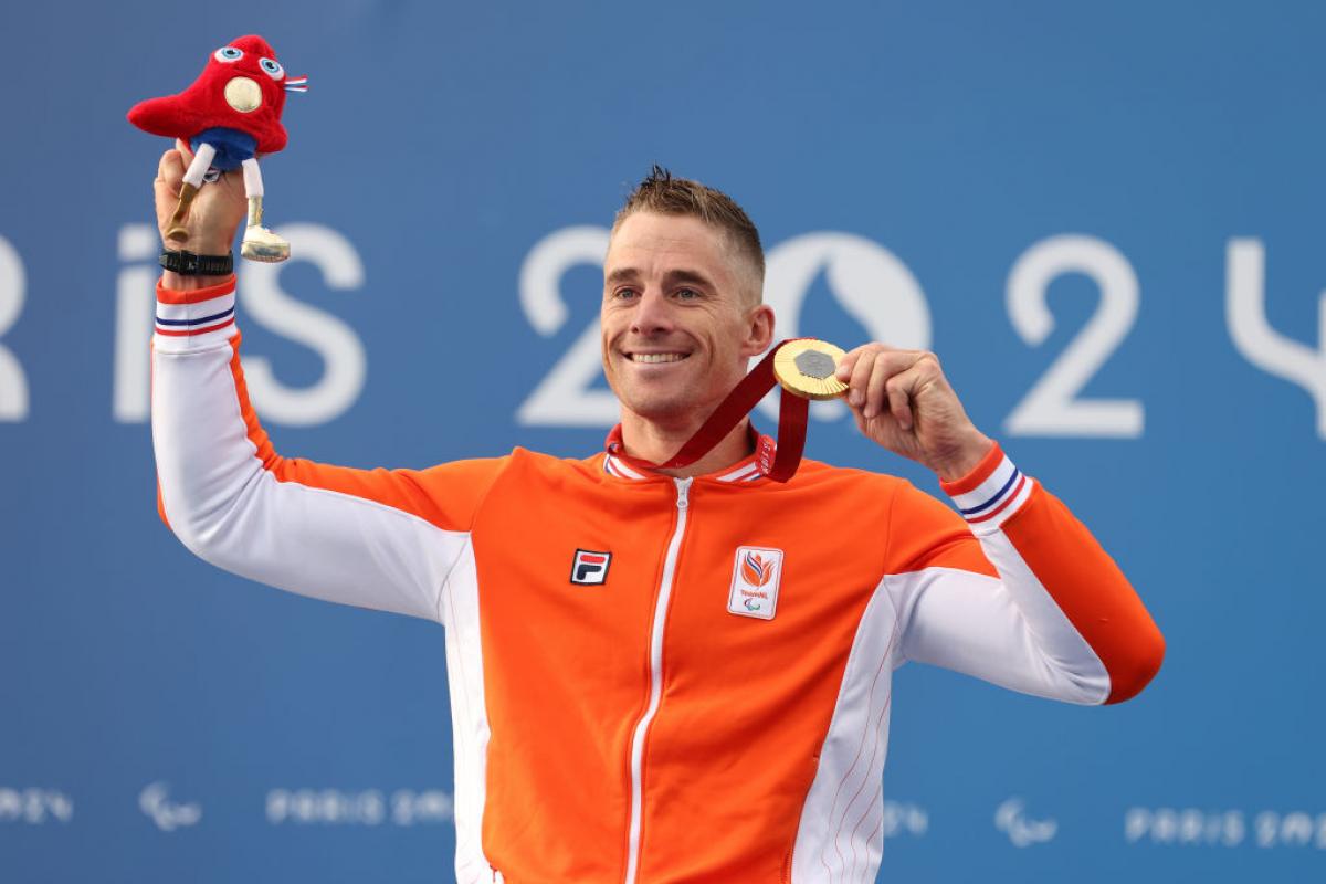 Para cyclist Jetze Plat holding up a gold medal and smiling