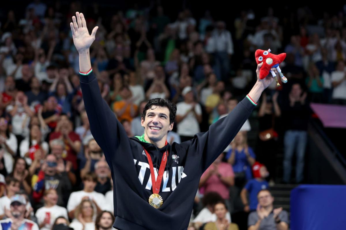 A man in a Team Italy sweater wearing a gold medal raises his arms in the air in celebration in front of a crowd of people at La Defense Arena
