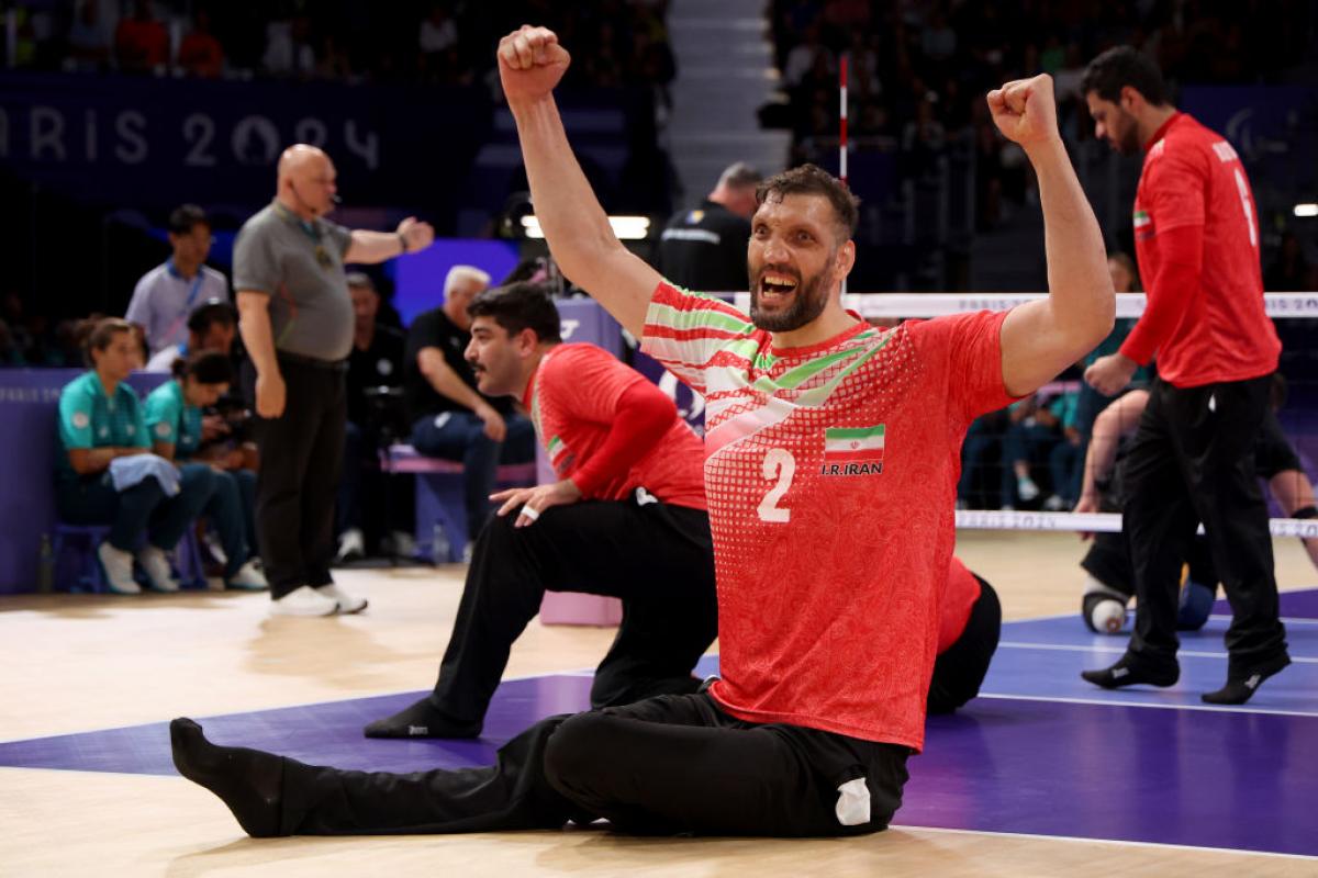 A sitting volleyball player raises his arms in celebration while on the volleyball court