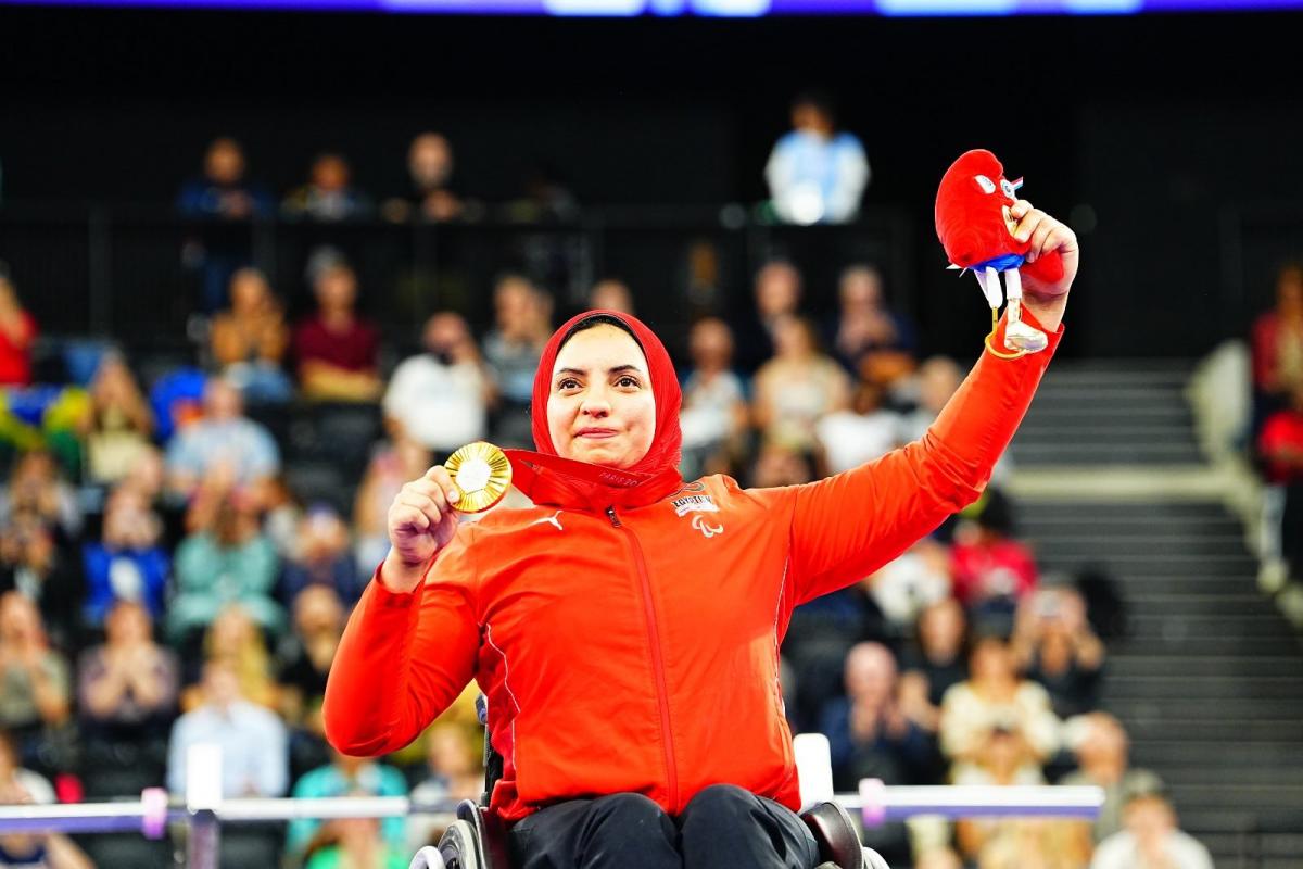 A woman in a wheelchair showing her medal to the public in an arena