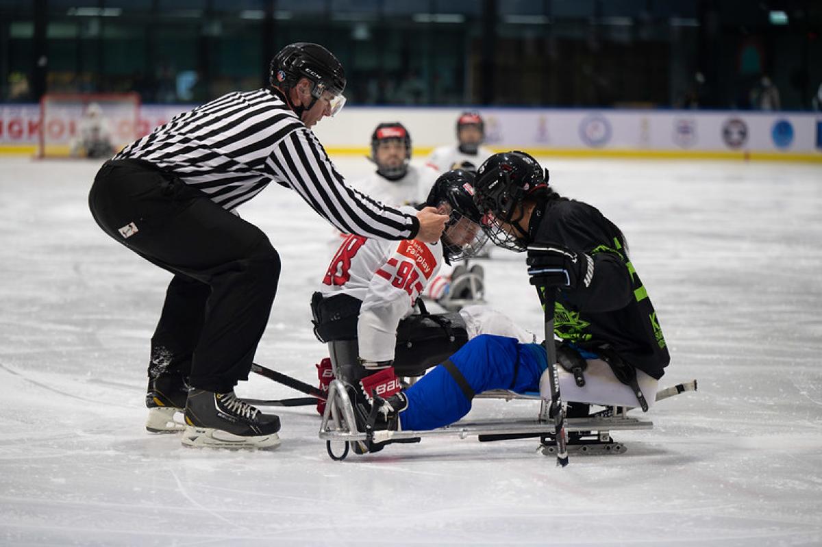 A Para ice hockey official dropping the puck in front of two players
