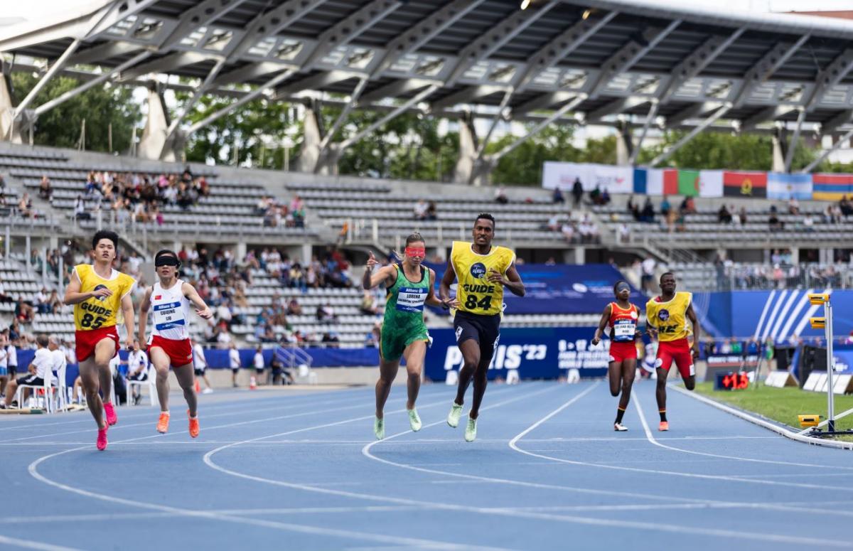 Three female runners with male guides in a Para athletics race