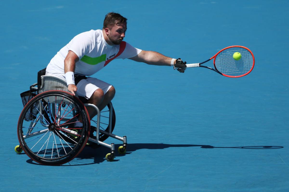 A male wheelchair tennis player reaches to return a shot