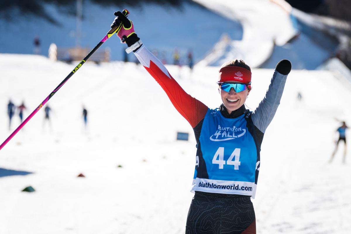 A female Para athlete wearing a ski gear raises her arms