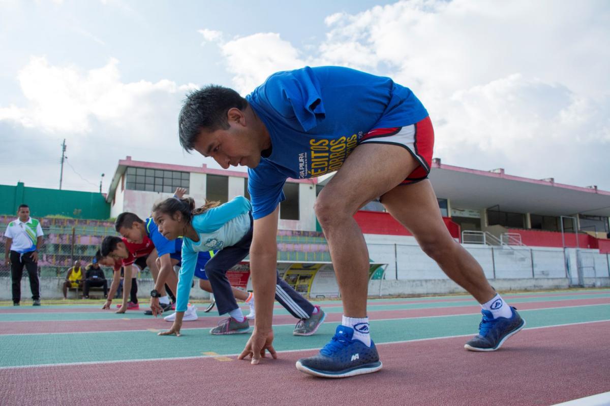 Five boys and girls with disabilities are bending down at the start line before racing at an outdoor track