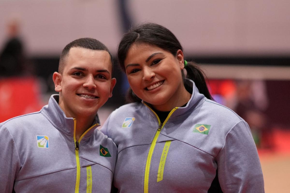 A male athlete and a female athlete pose for a photo together. They are wearing Brazil's gray jersey