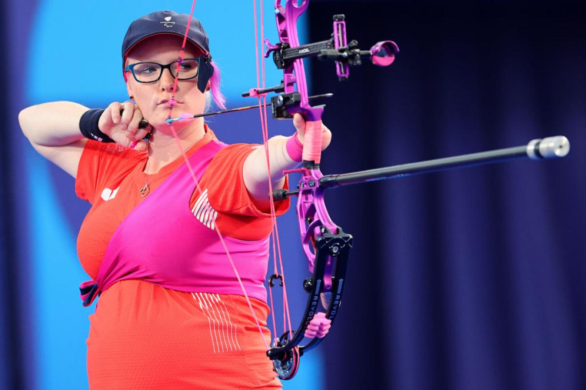 A female Para archer who is wearing a red T-shirt is aiming her bow while seven months pregnant