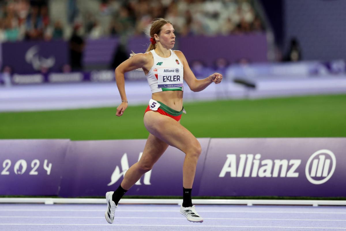 A female Paralympic sprinter competing at Paris 2024. Her bib has the logo of Allianz