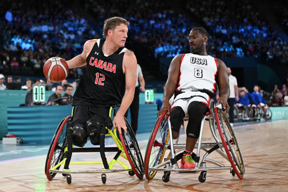 Two male wheelchair basketball players in action. The player in the left is dribbling the ball