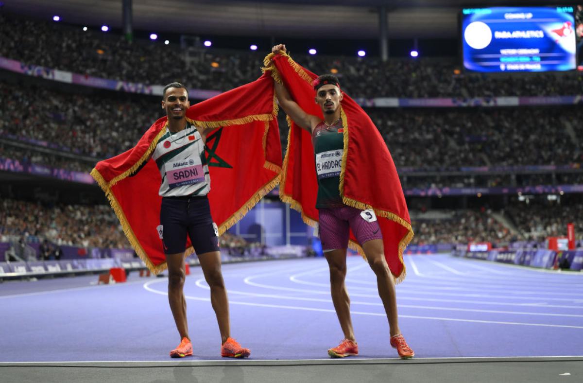 Two men with the Moroccan flag celebrating on the Stade de France athletics track