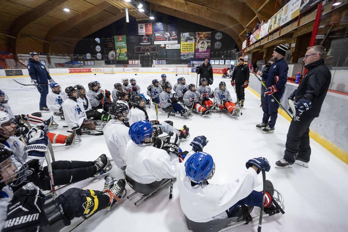 About four officials speaking in front of a group of Para ice hockey players