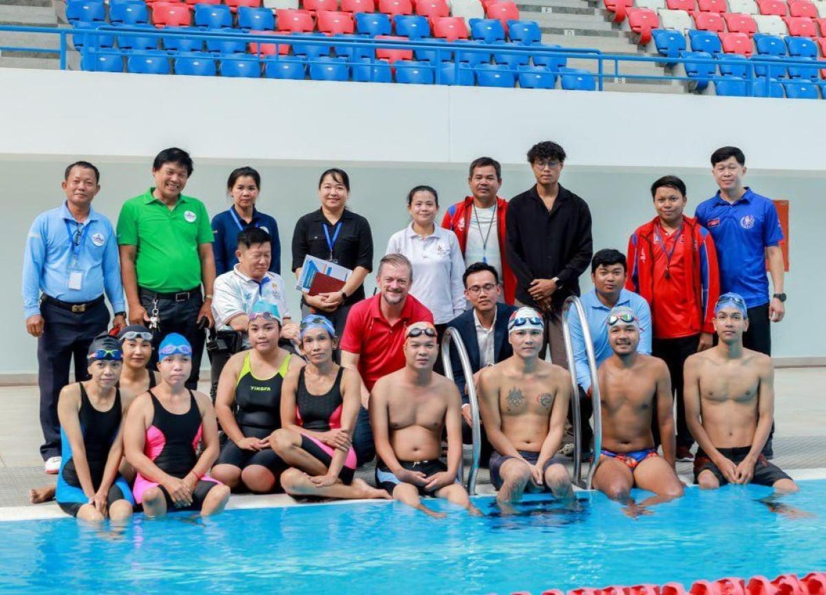 A group photo of about 20 people including swimmers and officials by the pool