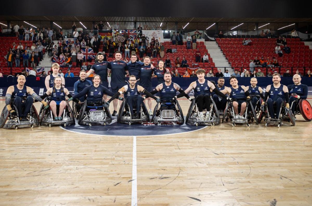 Seventeen people, including wheelchair rugby players and staff, pose for a group photo on a court