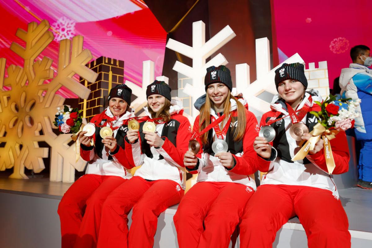 Four female athletes are posing for a photo while holding two medals each
