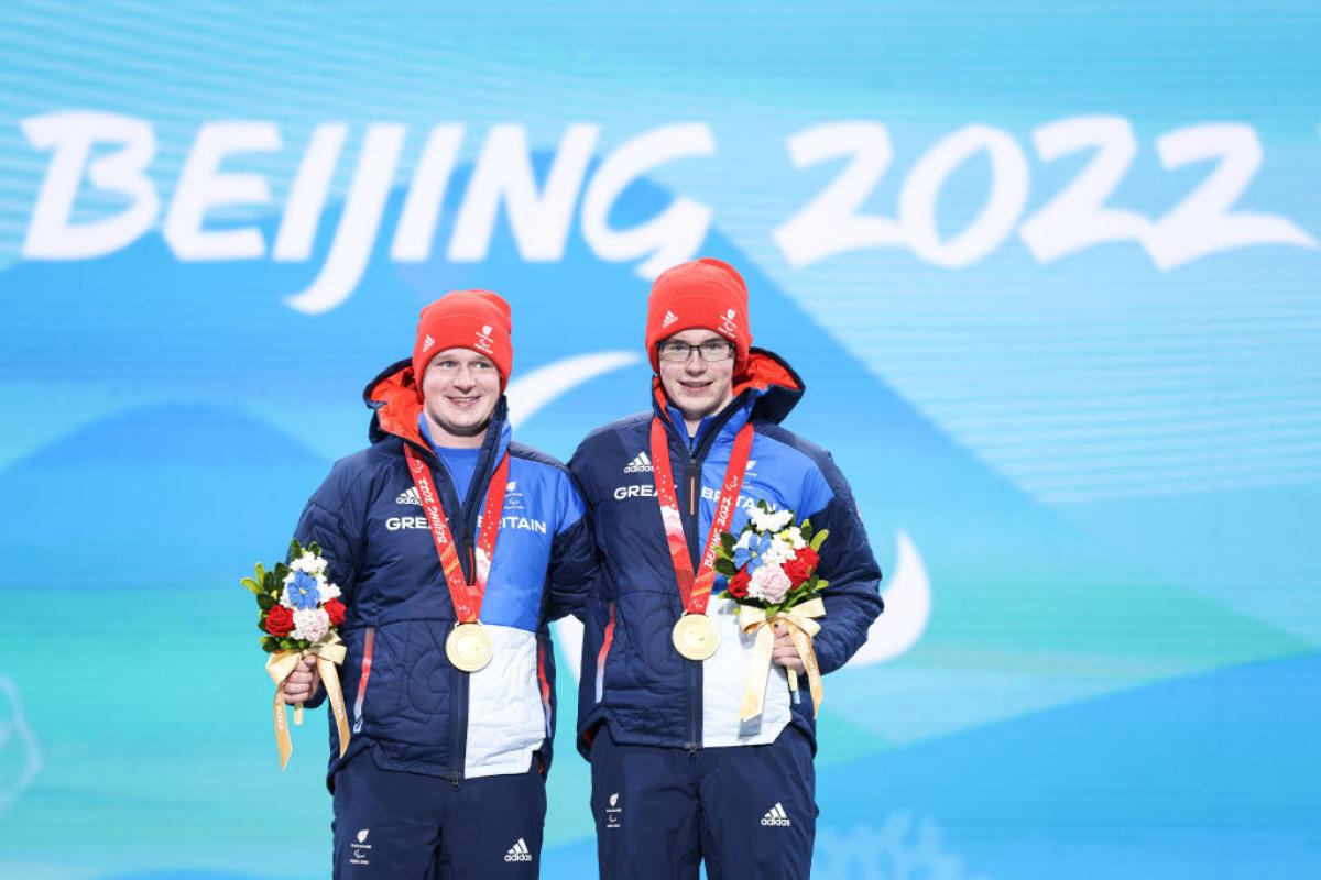 Two male athletes pose for a photograph on the podium after receiving gold medals
