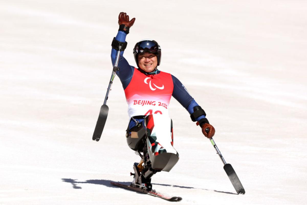 A male sit-skiing athlete is waving after a race