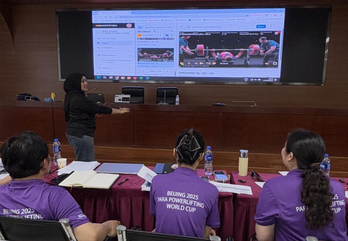 Three participants watching a woman make a presentation on a screen