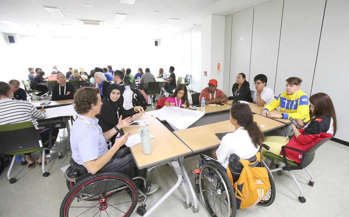 Nine athletes gather around a table for a discussion during the athletes' forum in 2023