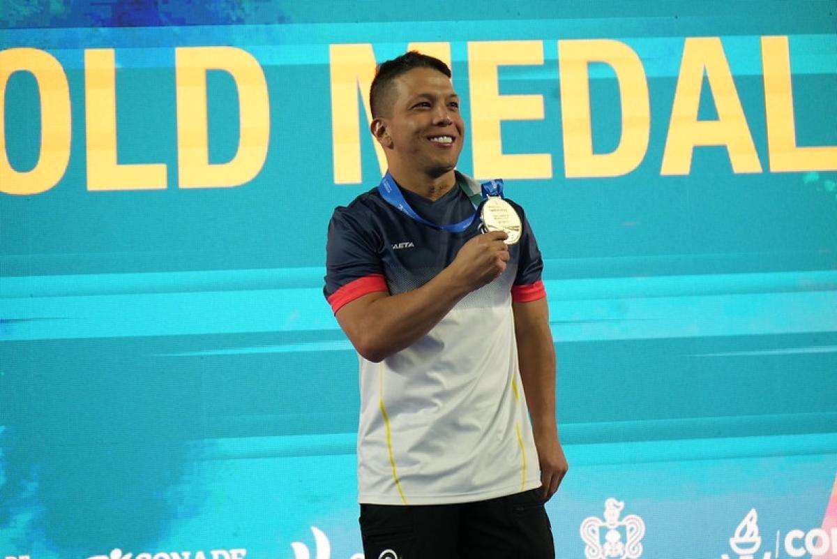 A man showing his medal with a backdrop with the words gold medal behind him