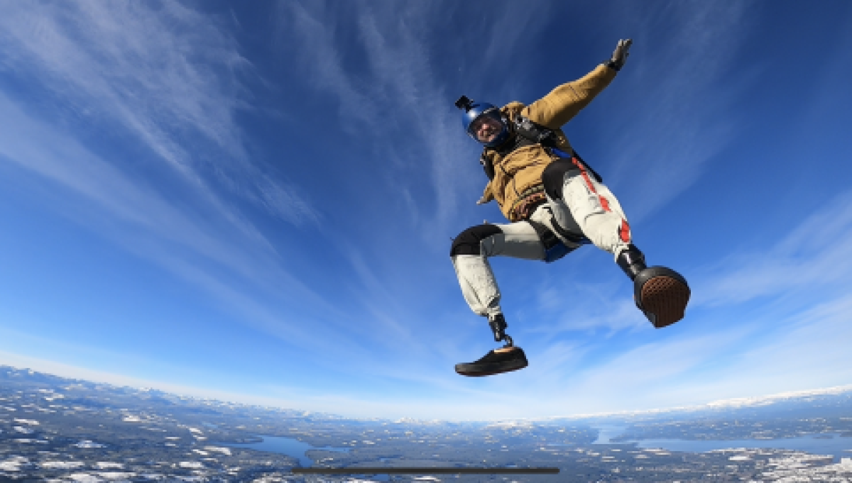 A male athlete is posing for a photo by opening his arms wide while skydiving